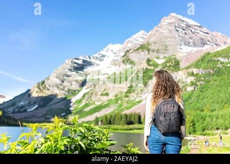 Aspen Maroon Bells rocky mountain peak with Creater Lake water in Colorado in summer and back of young woman hiker with backpack standing on trail Stock Photo