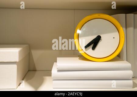 Yellow clock on the shelf. Copyspace. White books. Stock Photo