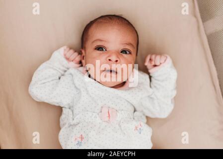 Dark-haired month old baby with wide open eyes lying in crib Stock Photo