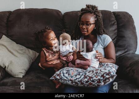 Ethnic mom in glasses on couch with multiracial daughter and newborn Stock Photo