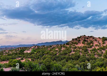 Sunset pink twilight in Santa Fe, New Mexico mountains Tesuque community neighborhood with houses green plants pignon trees shrubs and blue sky clouds Stock Photo