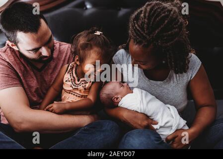 Multiracial parents holding smiling 2 yr old girl and swaddled baby Stock Photo