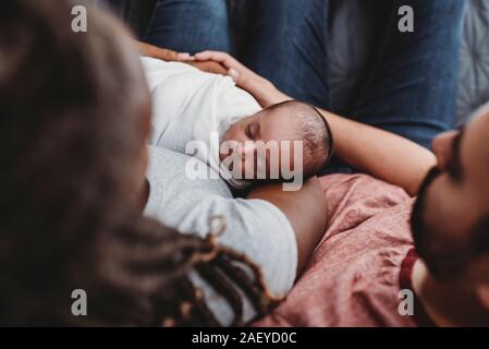 Mid-30â€™s multiracial couple holding their swaddled infant Stock Photo