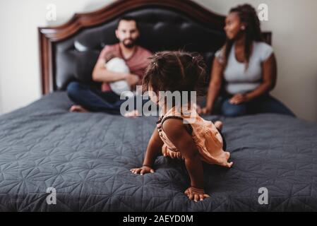In-focus multiracial girl on bed looking back at blurry family Stock Photo