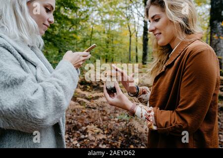 Women taking pictures of mushroom in a forest with a phone