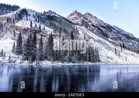 Maroon Bells morning reflection of pine trees in Aspen, Colorado rocky mountain closeup of winter snow frozen lake