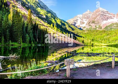 Maroon Bells lake at sunrise view in Aspen, Colorado with rocky mountain peak in July 2019 summer and reflection with sign to stay on trail on fence Stock Photo