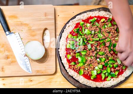 Flat top view down of raw pizza dough crust before baking made with gluten free flour and woman hands adding chopped green bell peppers on tomato sauc Stock Photo