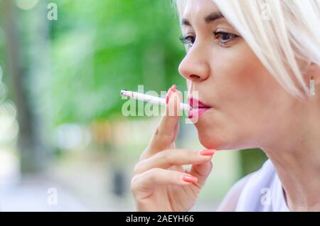A woman smokes a cigarette. Holds in the mouth, red lips Stock Photo