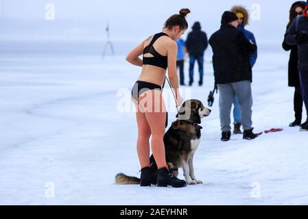 Winter sport, hardening in winter. A girl in a bathing suit with a dog stands near a river covered with ice and snow.  Orthodox holidayof Epiphany