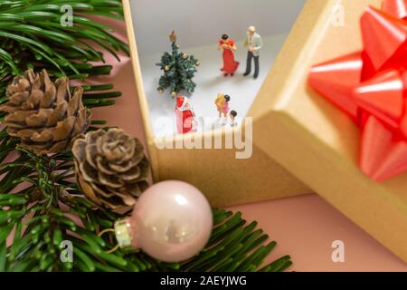 A miniature family is celebrating christmas in a small gift box decorated with a red ribbon and santa clause handing over presents Stock Photo