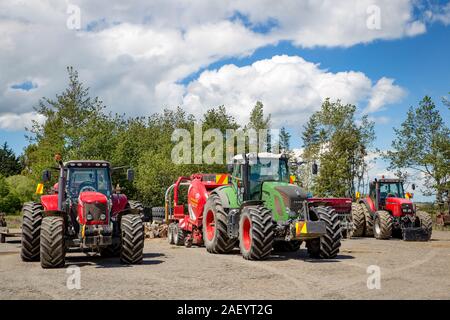 Otago, New Zealand, December 8 2019: Three tractors with mowing and baling machinery parked up in a contractor's yard between farm jobs