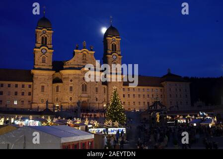 Einsiedler Weihnachtsmarkt (Christmas market) in front of the monastery Einsiedeln at dawn with a christmas tree, booths and the moon shining above. Stock Photo