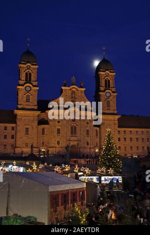 Einsiedler Weihnachtsmarkt (Christmas market) in front of the monastery Einsiedeln at dawn with a christmas tree, booths and the moon shining above. Stock Photo