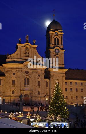 Einsiedler Weihnachtsmarkt (Christmas market) in front of the monastery Einsiedeln at dawn with a christmas tree, booths and the moon shining above. Stock Photo