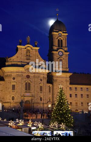 Einsiedler Weihnachtsmarkt (Christmas market) in front of the monastery Einsiedeln at dawn with a christmas tree, booths and the moon shining above. Stock Photo