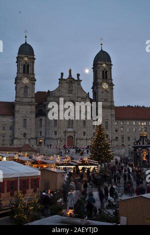 Einsiedler Weihnachtsmarkt (Christmas market) in front of the monastery Einsiedeln at dawn with a christmas tree, booths and the moon shining above. Stock Photo