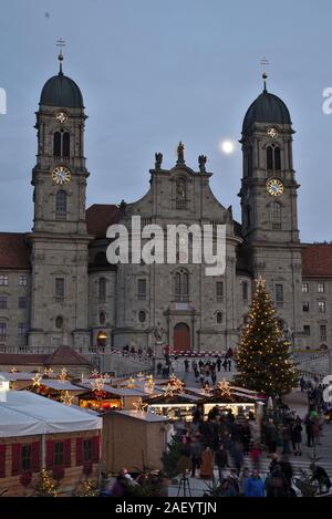 Einsiedler Weihnachtsmarkt (Christmas market) in front of the monastery Einsiedeln at dawn with a christmas tree, booths and the moon shining above. Stock Photo