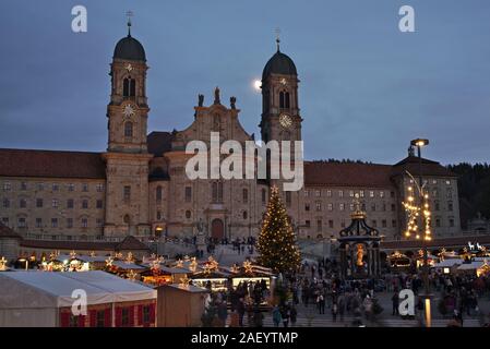 Einsiedler Weihnachtsmarkt (Christmas market) in front of the monastery Einsiedeln at dawn with a christmas tree, booths and the moon shining above. Stock Photo