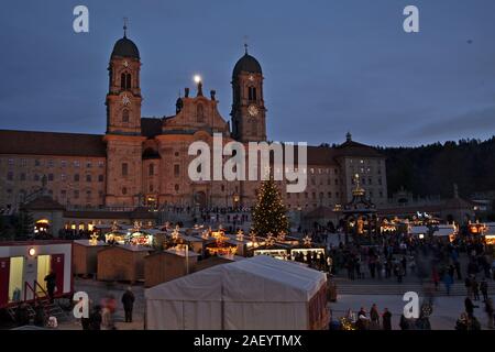 Einsiedler Weihnachtsmarkt (Christmas market) in front of the monastery Einsiedeln at dawn with a christmas tree, booths and the moon shining above. Stock Photo