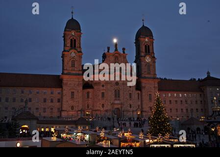 Einsiedler Weihnachtsmarkt (Christmas market) in front of the monastery Einsiedeln at dawn with a christmas tree, booths and the moon shining above. Stock Photo