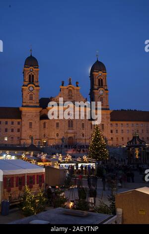 Einsiedler Weihnachtsmarkt (Christmas market) in front of the monastery Einsiedeln at dawn with a christmas tree, booths and the moon shining above. Stock Photo