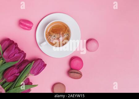 Creative spring composition with coffee, tulips and french dessert macarons on pink background, top view. Stock Photo