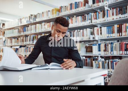 In stylish black shirt. African american man sitting in the library and searching for some information in the books Stock Photo