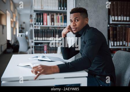 From the side. African american man sitting in the library and searching for some information in the books Stock Photo
