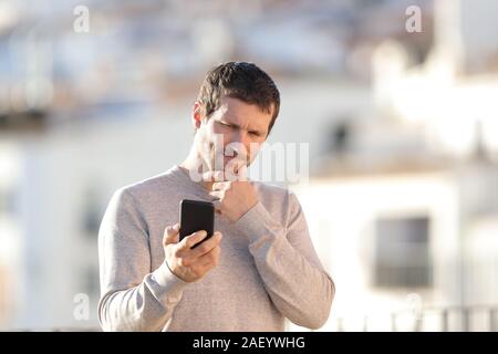 Doubtful adult man checking smart phone content standing in a rural town Stock Photo