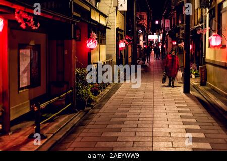 Kyoto, Japan - April 9, 2019: Narrow alley colorful red street in Gion district at night with people and illuminated lanterns Stock Photo