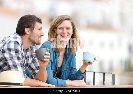 Happy couple talking drinking coffee standing outdoors in a balcony in a rural town Stock Photo