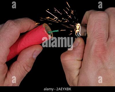 Close up of male hand lighting up a red firecracker on black background Stock Photo