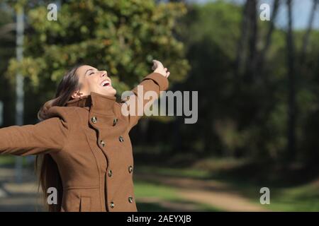 Excited woman wearing jacket outstretching arms in a park in winter Stock Photo