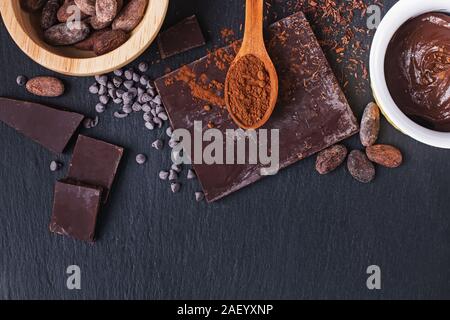Cocoa beans, powder and chocolate pieces on black slate background, top view Stock Photo
