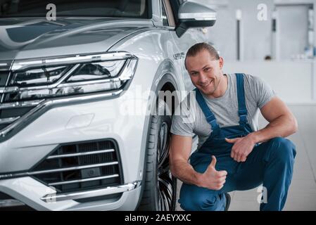 Showing thumb up. After professional repairing. Man looking at perfectly polished silver colored car Stock Photo