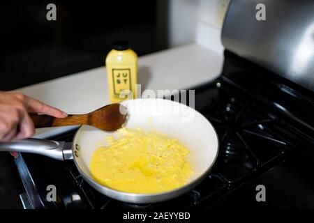 Aspen, USA - September 20, 2019: Woman cooking Just Egg substitute for scrambled omelette with wooden spatula in ceramic frying pan Stock Photo