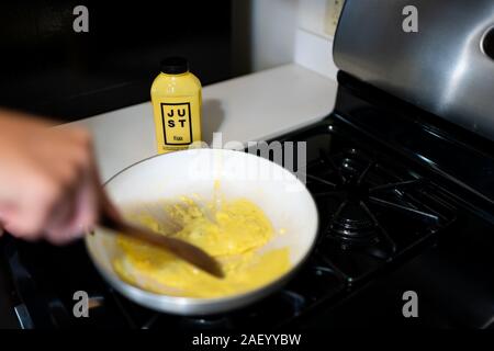 Aspen, USA - September 20, 2019: Woman cooking Just Egg substitute alternative for scrambled omelette with wooden spatula in ceramic frying pan Stock Photo