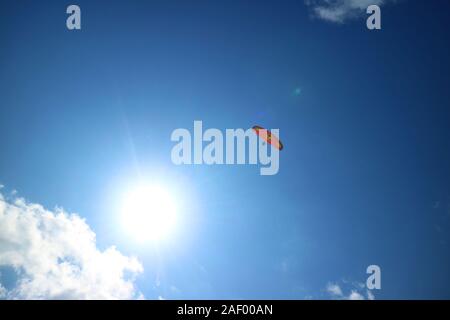 Red Paraglider Flying in the Blue Sky with the Dazzling Sun Stock Photo