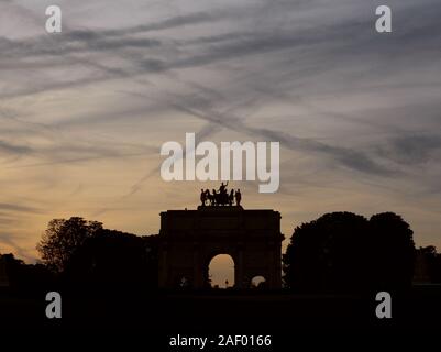 Arc de Triomphe du Carrousel near the Louvre in Paris in silhouette against a twilight sky covered in contrails