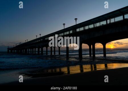 Sunset at Boscombe Pier, Bournemouth with pier in silhouette and rough sea with waves crashing into the beach. Stock Photo