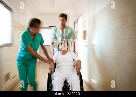 Doctor and nurse rushing a patient down a corridor in a wheelchair. Stock Photo