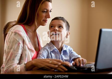 Woman using her laptop at home with her son. Stock Photo