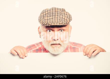 Elderly person. Announcement concept. Event announcement. Pensioner grandfather in vintage hat poster information copy space. Senior bearded emotional man peek out of banner place announcement. Stock Photo
