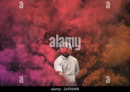 guy in mask standing in between pink, purple and orange smoke bombs Stock Photo