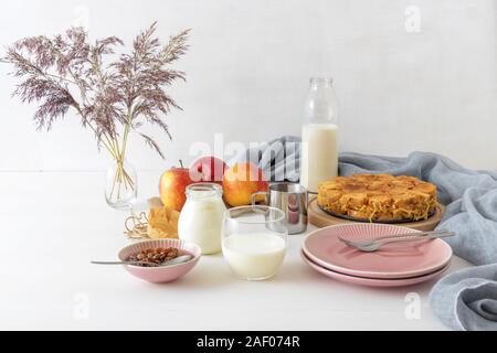 White wooden table with apple bread and butter pudding, jar with sour cream, glass of milk, background decorated with few apples and vase with dry gra Stock Photo