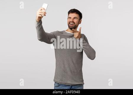 Cheeky, excited and carefree young man bearded, travel abroad photographing, posting pictures online, use application filters, hold smartphone upwards Stock Photo