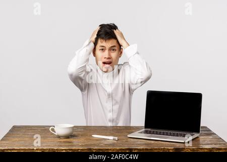 Guy having trouble, dont know what do, sitting indecisive and anxious. Shocked and distressed asian businessman panic, grab head troubled and Stock Photo