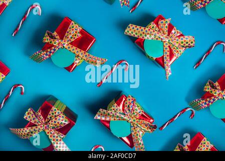 Bright gift boxes pattern. Top view set of red presents with golden bows and turquoise blank cards with christmas candy canes on trendy blue backgroun Stock Photo