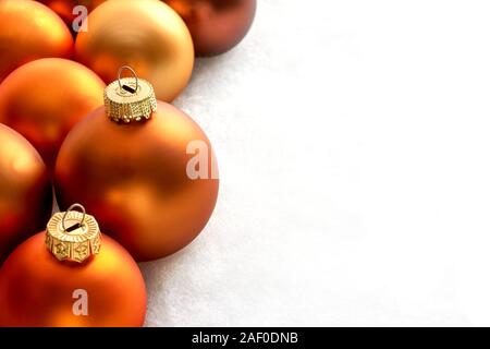 Mat bronze orange colored chtristmas balls on a white snowy background for use as a christmas card template with copy space. Stock Photo